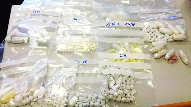 Mehrere Plastiktüten mit Pillen und Pulvern unterschiedlicher Art liegen auf einem Tisch.