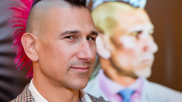 Ein Mann mit einem pinkfarbenen Irokesenschnitt lächelt in die Kamera.