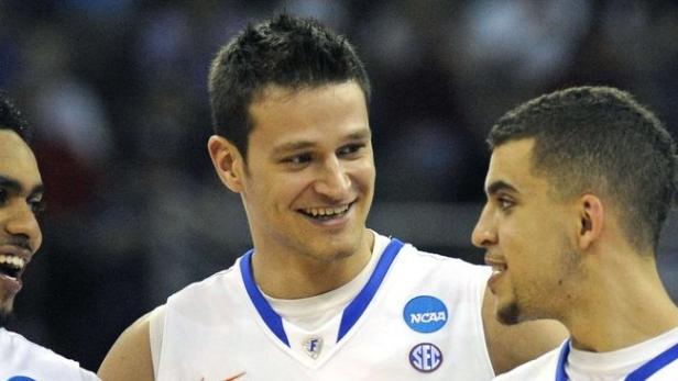 Drei Basketballspieler in weißen Trikots mit NCAA-Logos lächeln.