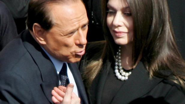 Silvio Berlusconi im Gespräch mit einer Frau mit Perlenkette.
