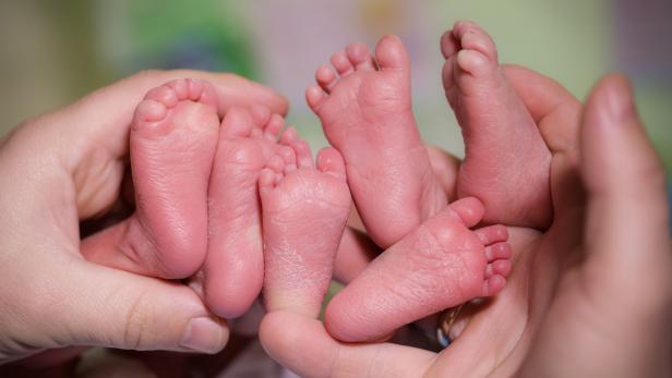 A mother is holding in the hands feet of newborn triplets baby.
