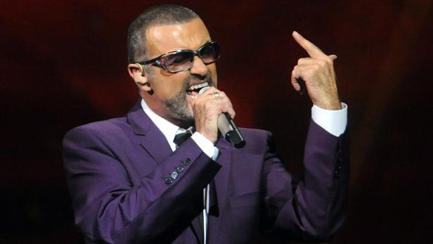 George Michael singt in einem lila Anzug auf der Bühne.