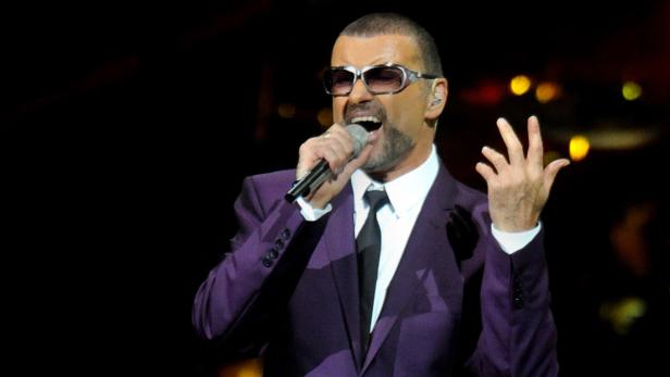 George Michael singt in einem lila Anzug auf der Bühne.