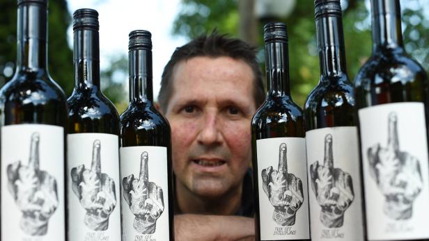 Ein Mann steht hinter mehreren Weinflaschen mit provokanten Etiketten.