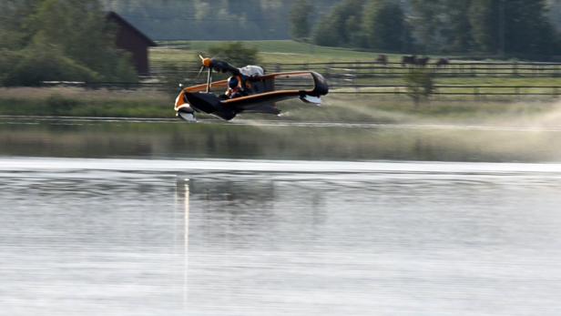 Ein Tragschrauber fliegt über die Oberfläche eines Sees.