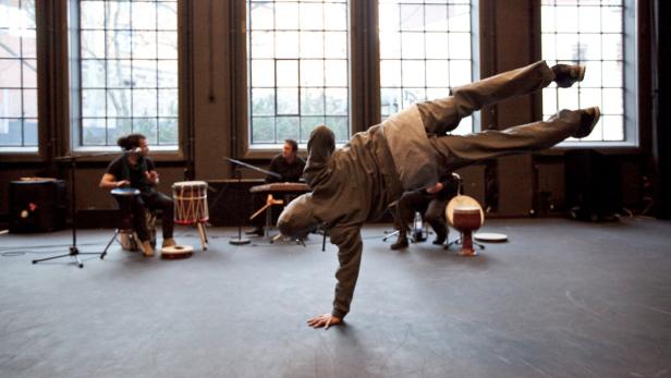 Ein Mann macht einen Handstand vor einer Band, die auf der Bühne musiziert.