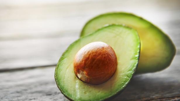 Eine halbierte Avocado mit großem Kern liegt auf einer Holzfläche.