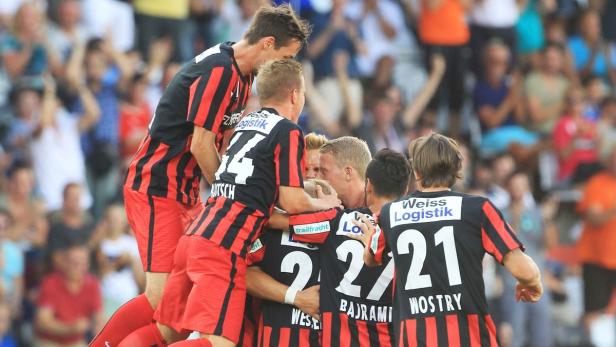 Eine Gruppe von Fußballspielern umarmt sich auf dem Spielfeld, während die Fans im Hintergrund jubeln.