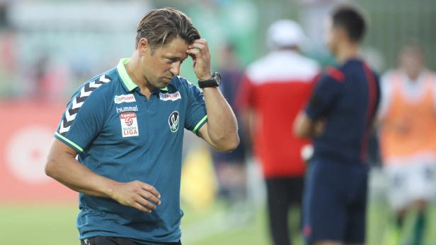 Ein Fußballtrainer steht nachdenklich auf dem Spielfeld.