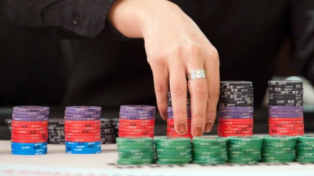 Eine Hand mit einem Ring greift nach einem Stapel Pokerchips.