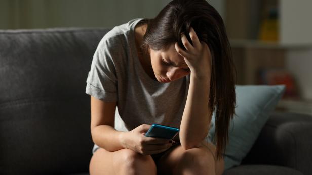 Eine junge Frau schaut traurig auf ihr Handy.