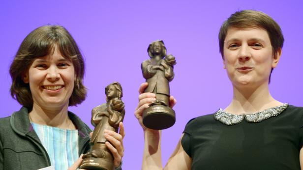 Zwei Frauen halten Statuen des Deutschen Jugendliteraturpreises in die Höhe.