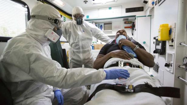 Rettungssanitäter in Schutzkleidung versorgen einen Patienten in einem Krankenwagen.
