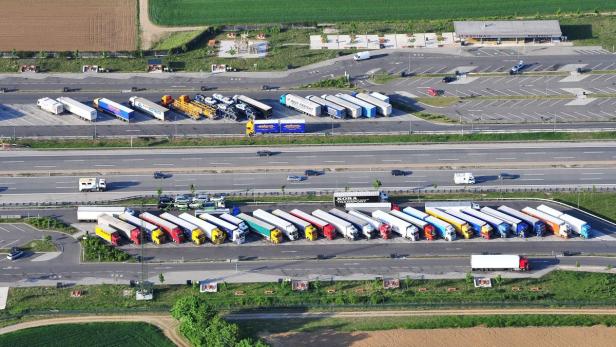 Ein Autobahnparkplatz mit vielen parkenden Lastwagen und einem Rasthof.