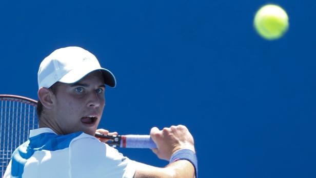 Ein Tennisspieler mit weißer Kappe schlägt einen Tennisball.