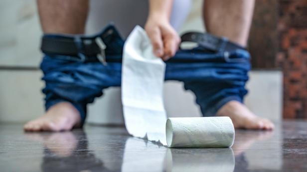 Mann auf der Toilette, ihm rollt das WC-Papier davon.