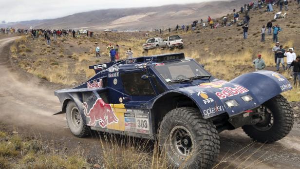 Ein Red Bull Rallye-Auto fährt auf einer staubigen Straße vor einer Menschenmenge.