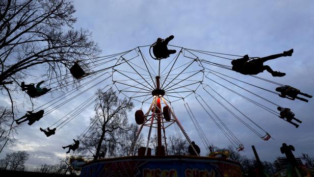 People sit on a swing carousel ride at St. Matthew's fairground, a traditional amusement park, in Prague