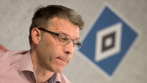 Ein Mann mit Brille und gestreiftem Hemd vor dem Logo des Hamburger SV.