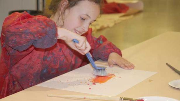 Ein Mädchen malt mit einer Bürste auf einem Blatt Papier.