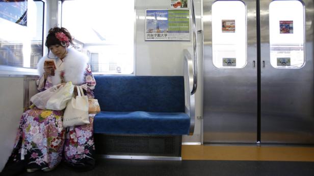 Eine junge Frau im Kimono sitzt in einem Zug und benutzt ihr Smartphone.