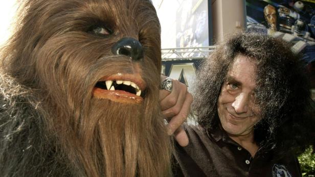 Ein Mann mit lockigem Haar posiert neben einer Chewbacca-Figur.