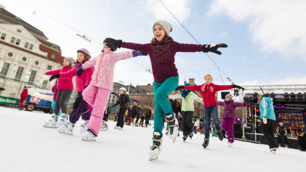 Eine Gruppe von Kindern übt gemeinsam Eislaufen auf einer Eisbahn.