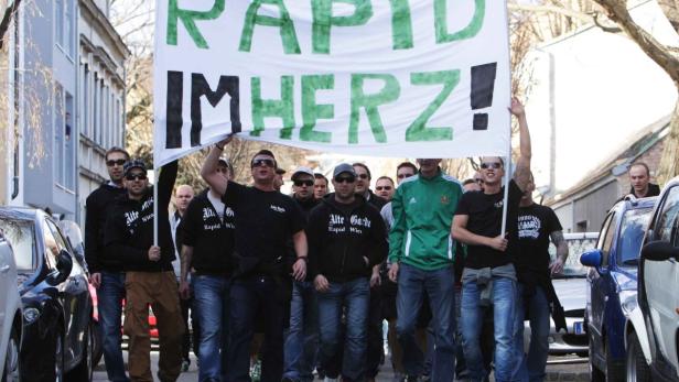 Eine Gruppe von Rapid Wien Fans demonstriert mit einem Transparent auf der Straße.