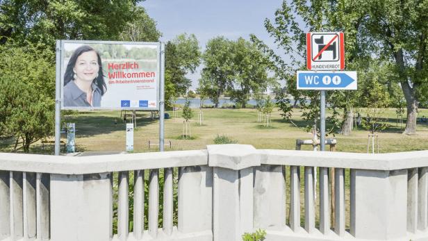 Ein Park mit einem Schild, das für den Arbeiterinnenstrand wirbt, und einem Hinweisschild für Toiletten.