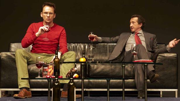 Zwei Männer sitzen auf einem Sofa und trinken Wein.