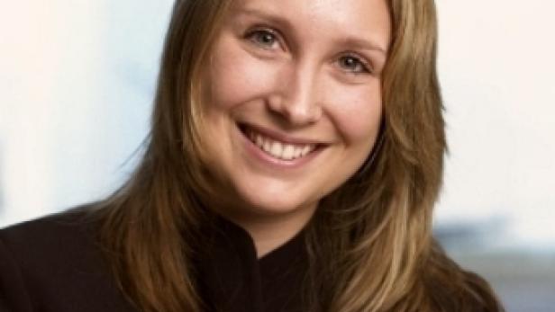Eine lächelnde Frau mit blonden Haaren und dunklem Blazer.
