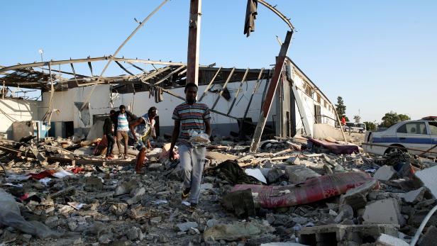 Migrants carry the remains of their belongings from among rubble at a detention centre for mainly African migrants that was hit by an airstrike in the Tajoura suburb of the Libyan capital of Tripoli