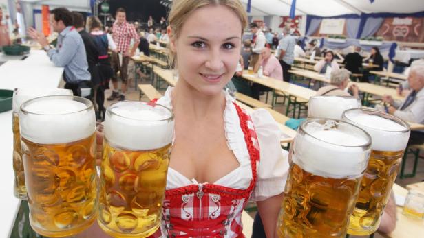 Eine junge Frau im Dirndl trägt mehrere volle Bierkrüge.