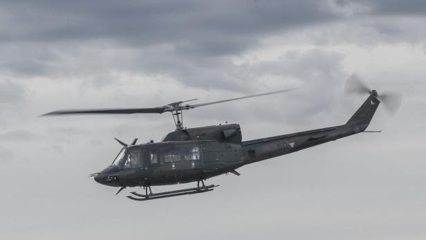 Ein grauer Militärhubschrauber fliegt vor einem bewölkten Himmel.