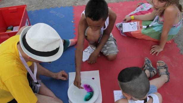 Kinder und ein Erwachsener experimentieren mit Farben in einer Schüssel.