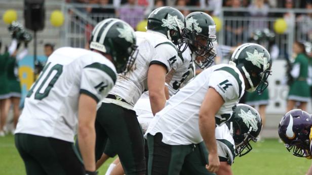 Eine Gruppe von American-Football-Spielern in weißen und grünen Uniformen steht auf dem Spielfeld.
