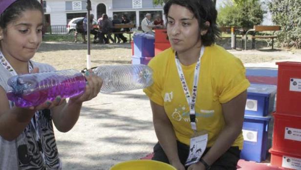 Ein Mädchen hält eine mit violetter Flüssigkeit gefüllte Plastikflasche hoch, während eine Betreuerin zusieht.