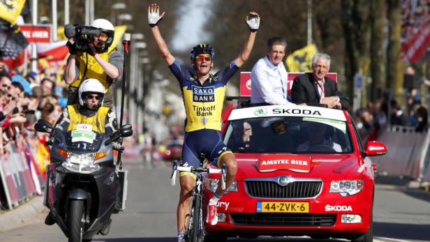 Ein Radrennfahrer jubelt mit erhobenen Armen vor einem roten Škoda-Begleitfahrzeug.