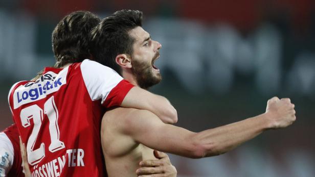 Ein jubelnder Fußballspieler wird von einem Teamkollegen umarmt.