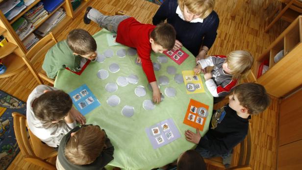 Eine Gruppe Kinder sitzt mit einer Erzieherin an einem Tisch und spielt ein Spiel.