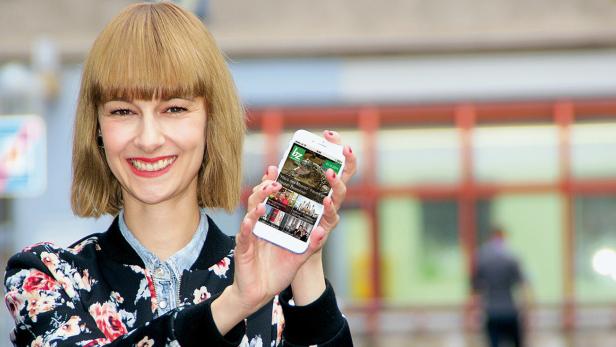 Eine lächelnde Frau präsentiert die Nachrichten-App „bz“ auf ihrem Smartphone.