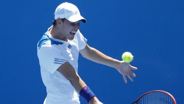 Ein Tennisspieler schlägt einen Ball vor einem blauen Hintergrund.