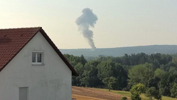 Rauch steigt in der Ferne über einem bewaldeten Gebiet auf.