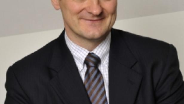 Ein Mann in Anzug und Krawatte lächelt in die Kamera.