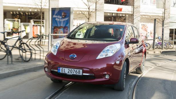 Ein roter Nissan Leaf fährt auf einer Straße mit Straßenbahnschienen.