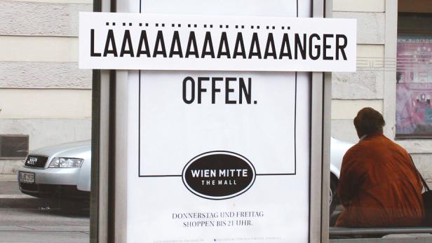 Eine Frau sitzt an einer Bushaltestelle mit Werbung für „Wien Mitte The Mall“.