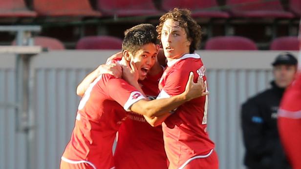 Drei Fußballspieler in roten Trikots umarmen sich jubelnd.