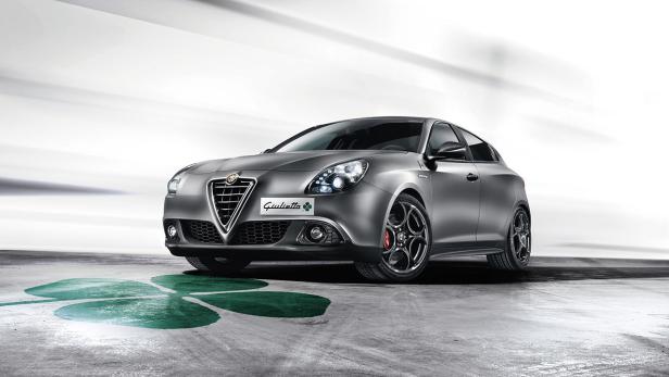 Ein grauer Alfa Romeo Giulietta vor einem weißen Hintergrund mit einem grünen Kleeblatt auf dem Boden.