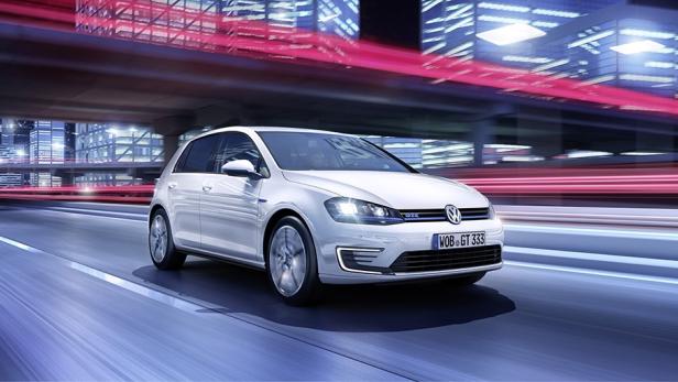 Ein weißer VW Golf fährt auf einer Straße in einer nächtlichen Stadt.