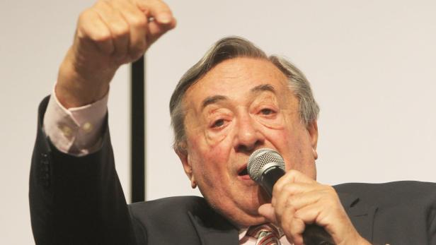 Ein älterer Mann mit Mikrofon gestikuliert mit erhobener Faust.